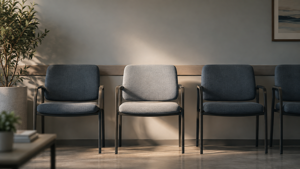 A row of empty clinic waiting room chairs with one chair lit, representing the fertility appointment many men never make.