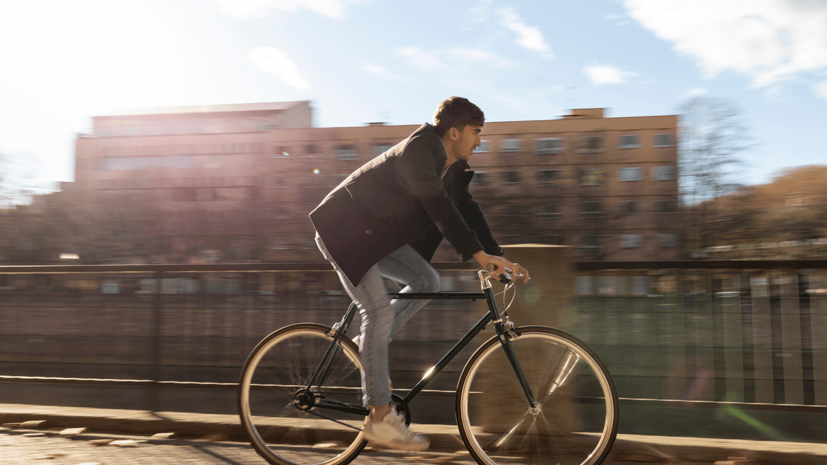 A young man in casual clothing rides a bicycle outdoors on a sunny day, representing the link between cycling and male fertility.