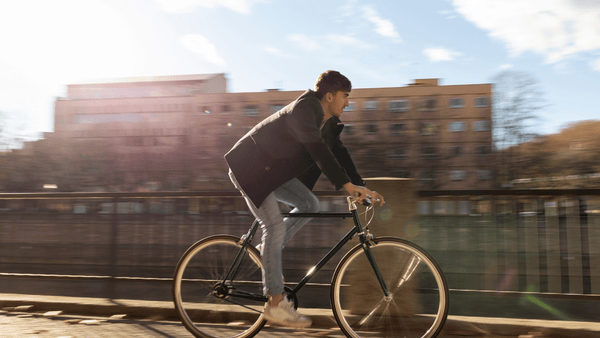 A young man in casual clothing rides a bicycle outdoors on a sunny day, representing the link between cycling and male fertility.
