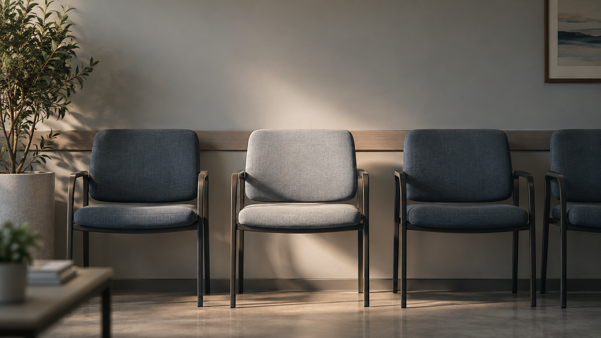 A row of empty clinic waiting room chairs with one chair lit, representing the fertility appointment many men never make.