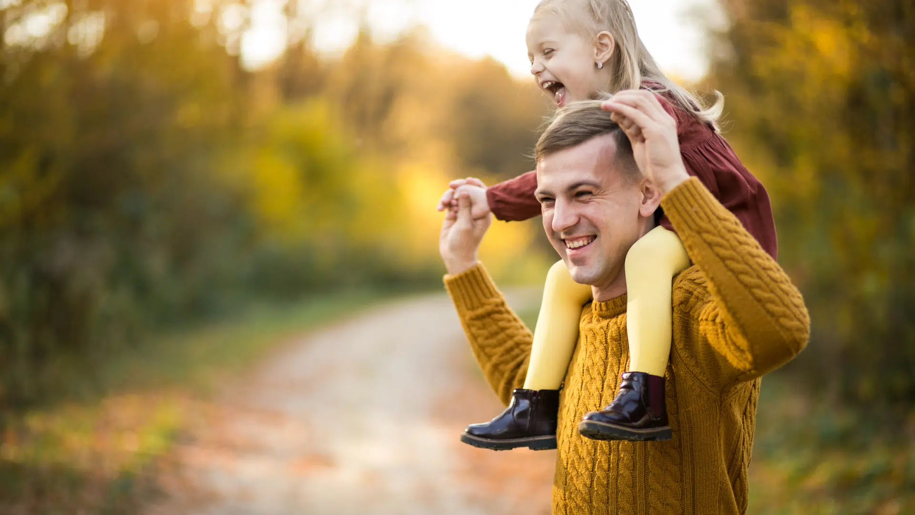 Smiling father carrying his joyful daughter on his shoulders during a walk in nature, representing vitality, longevity, and family health.